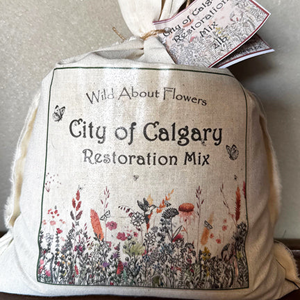 A cloth bag labeled "City of Calgary Restoration Mix" from Wild About Flowers sits against a neutral background. The design features delicate illustrations of native wildflowers, grasses, and butterflies, capturing the essence of prairie restoration. A matching tag is tied to the top, emphasizing the mix’s local, eco-friendly focus.